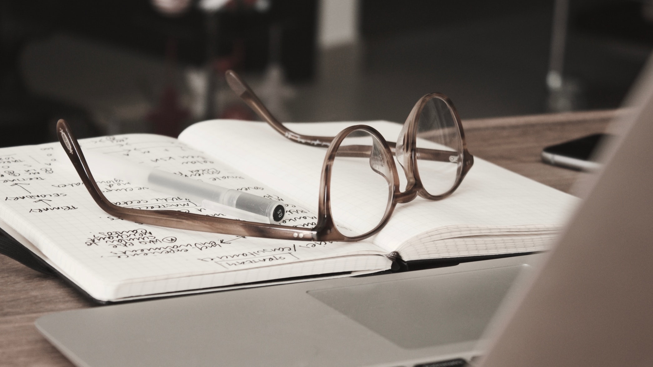 Glasses sitting on an open notebook in front of a laptop